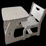 Concrete table and chair set on a concrete floor with a colorful wall in the background.